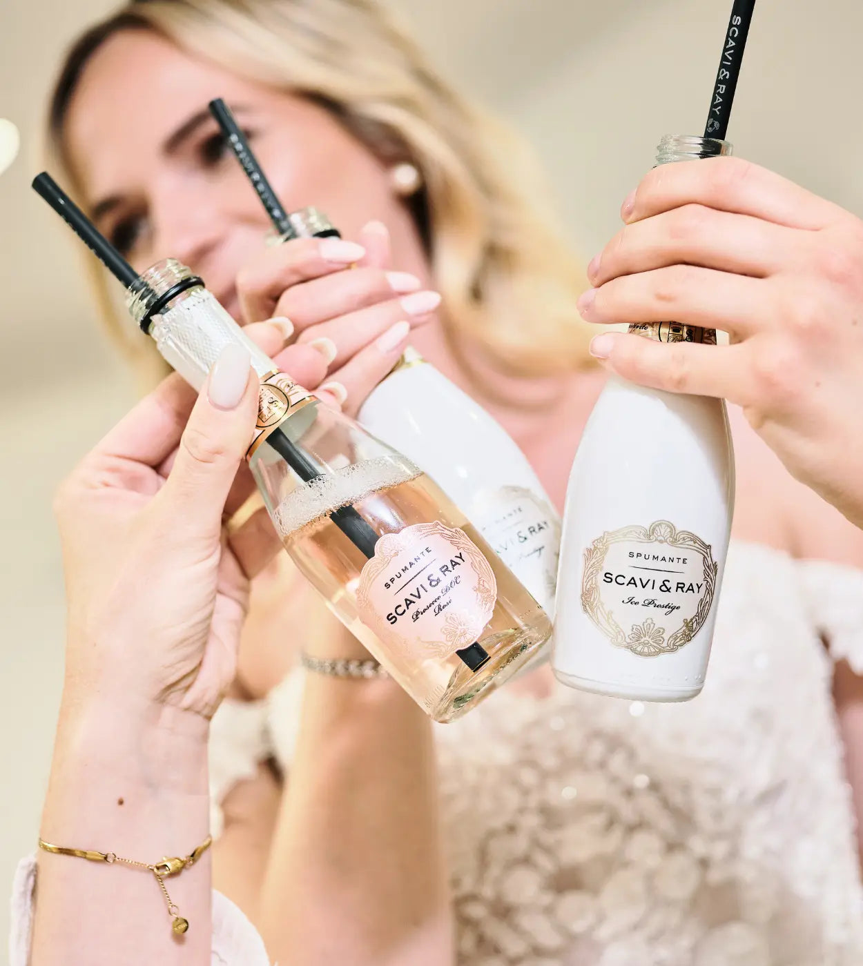Drei SCAVI & RAY Mini-Flaschen mit Strohhalmen werden angestoßen, im Hintergrund ist eine Person in einem weißen Kleid zu sehen.